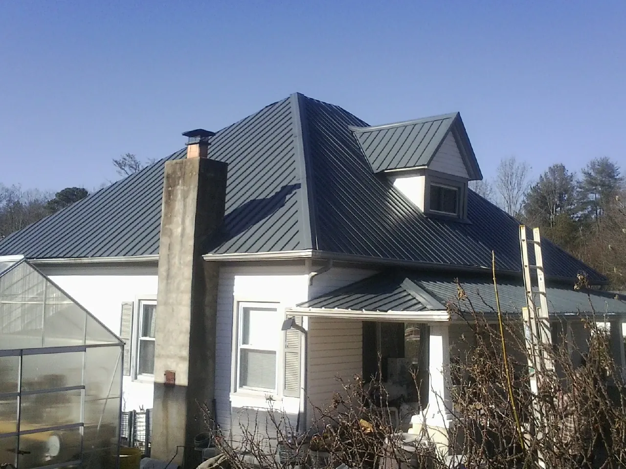Dark blue standing seam metal roof on a white farmhouse with dormer — Slate & Tile Roof Repair by Roofing Brothers in Lone Oak