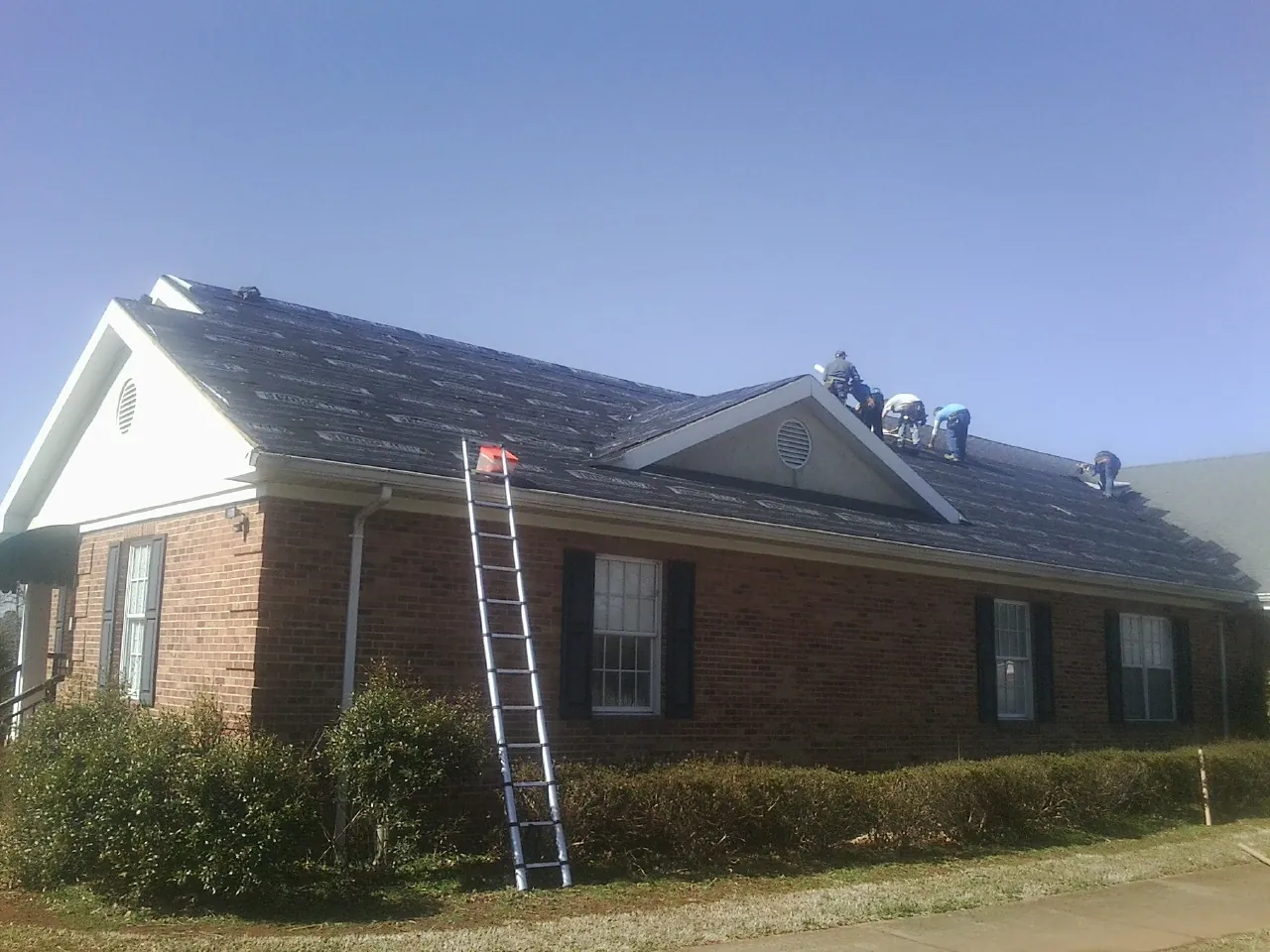 Crew tearing shingles off a brick ranch roof with a ladder set — Emergency Roof Repair work by our crew in Lone Oak