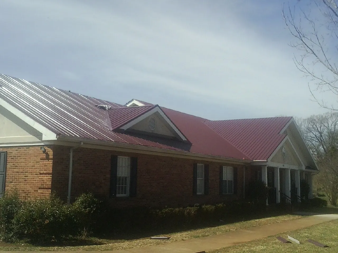 Red metal roof with gabled entries on a long brick building, from a Hail Damage Roof Repair job in Lone Oak