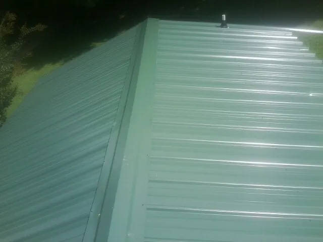 New green metal panels meeting at the ridge of a roof — Flat Roof Repair work by our crew in Lone Oak