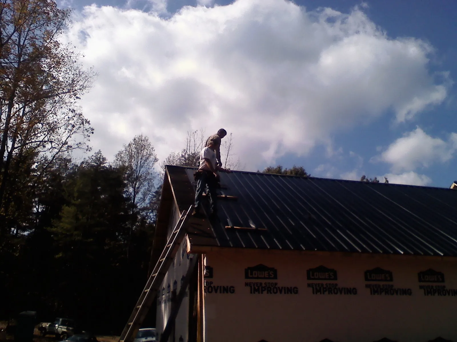 Roofer fastening dark metal panels high against a cloudy sky, from a Roof Inspection job in Lone Oak