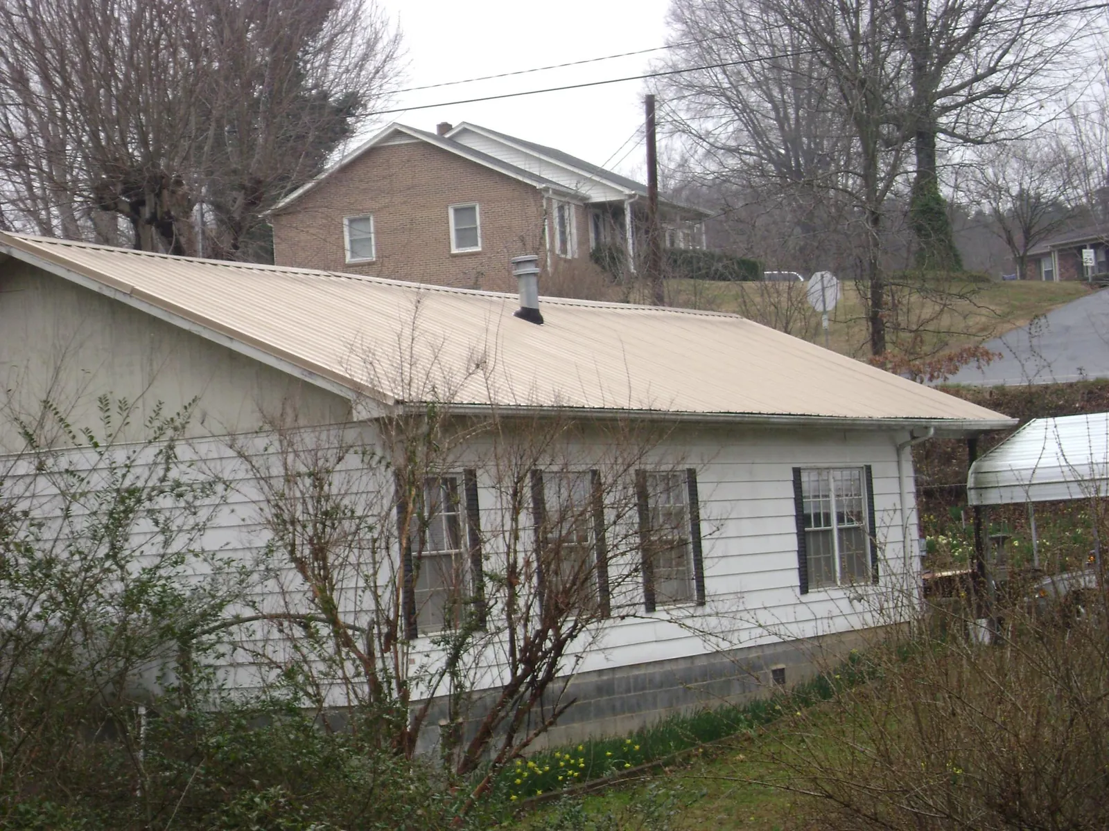 Tan metal roof on a white sided house set into a hillside — Commercial Roofing by Roofing Brothers in Lone Oak